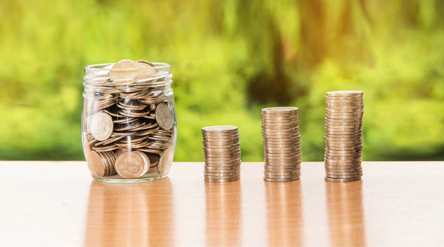 Ein Glas gefüllt mit Münzen und mehrere Münzstapel, die eine Lohnanalyse und die Bewertung der Lohngerechtigkeit symbolisieren.